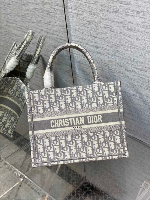 DIOR Book Tote. Original Quality Bag including gift box, care book, dust bag, authenticity card. This Book Tote is an original style introduced by Creative Director Maria Grazia Chiuri. This has become a staple of the Dior aesthetic. Ideally designed to carry all your daily essentials, the small shape is fully embroidered and the 'Christian Dior' signature on the front. This carryall is a perfect example of the Dior savoir-faire and also may be coordinated with a pouch or other small leather goods for a complete look. | CRIS&COCO Authentic Quality Designer Bags and Luxury Accessories