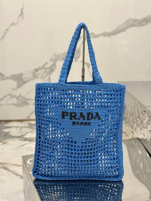 PRADA Crochet Tote Bag. Elevate your style with Prada's signature tote bag. This tote bag is the perfect addition to any summer wardrobe! Adorned with Prada's iconic triangle logo and embroidered lettering, its soft, deconstructed design is made with a light and natural raffia-effect yarn. It's sure to add an elevated touch to your ensemble. | CRIS&COCO Authentic Quality Designer Bags and Luxury Accessories