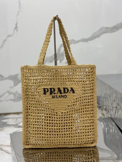 PRADA Crochet Tote Bag. Elevate your style with Prada's signature tote bag. This tote bag is the perfect addition to any summer wardrobe! Adorned with Prada's iconic triangle logo and embroidered lettering, its soft, deconstructed design is made with a light and natural raffia-effect yarn. It's sure to add an elevated touch to your ensemble. | CRIS&COCO Authentic Quality Designer Bags and Luxury Accessories