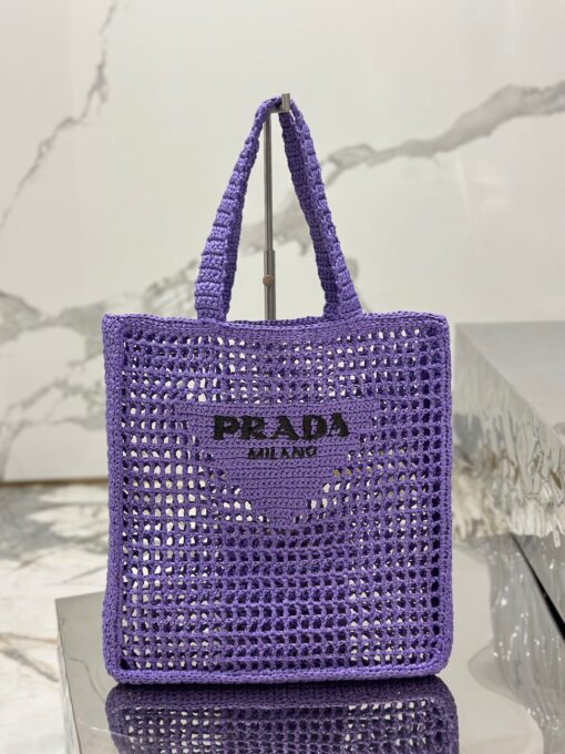 PRADA Crochet Tote Bag. Elevate your style with Prada's signature tote bag. This tote bag is the perfect addition to any summer wardrobe! Adorned with Prada's iconic triangle logo and embroidered lettering, its soft, deconstructed design is made with a light and natural raffia-effect yarn. It's sure to add an elevated touch to your ensemble. | CRIS&COCO Authentic Quality Designer Bags and Luxury Accessories