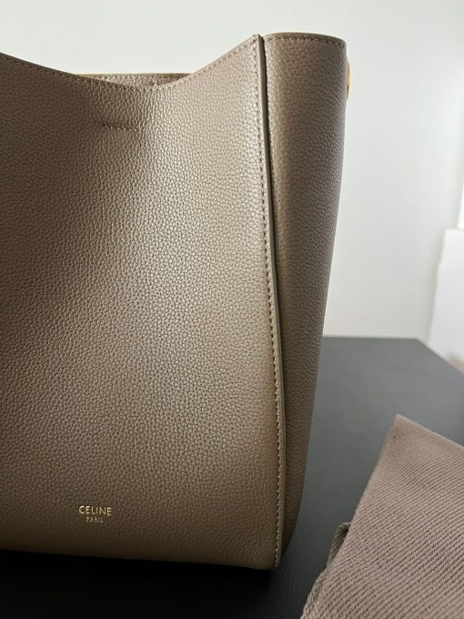 CELINE Sangle Small Bucket Bag. Elevate Your Style with Elegance and Versatility. The Sangle Small Bucket Bag is a stylish and versatile handbag made from high-quality calfskin leather. It offers the option of using a removable wool shoulder strap for convenient carrying and features an inner hook closure to keep your items secure. This description highlights both the design and practicality of the bag, making it a fashionable and functional accessory.