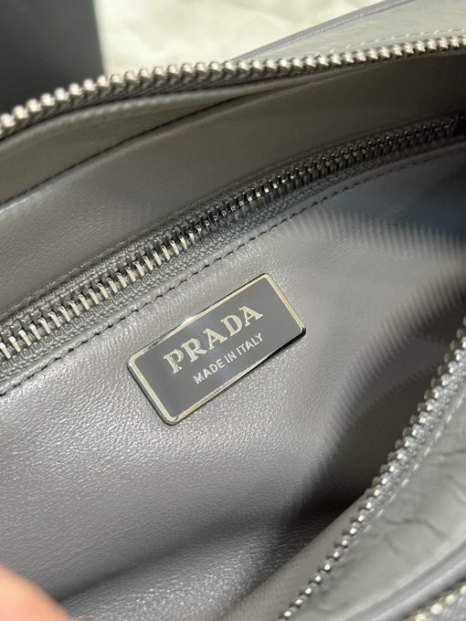 PRADA Nappa Antique Leather Shoulder Bag. High-End Quality Bag including gift box, care book, dust bag, authenticity card. This bag with compact allure is made of nappa leather with a natural, glossy finish. The hand-made wrinkled effect contrasts with the constructed and rigid concept, reinterpreting an everyday object to be worn without constraints. Presented in the Spring Summer 2023 show, the style is accented with a finely embroidered shoulder strap with a sporty mood.