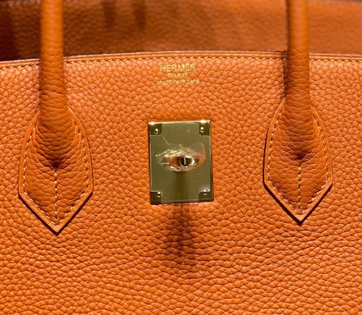 HERMÈS Birkin. Exquisite Craftsmanship and Timeless Elegance: Discover the Allure of the HERMES Birkin Bag Large Leather Top Handle. Designed with the actress Jane Birkin in mind, the Birkin bag is a contemporary development of the Kelly bag. Created based on Jane's suggestions, it was architected to be more significant to fit modern women's fast-paced life, with several minor yet outstanding adaptations, such as the elongated top handles. The French Birkin 30 bag is a classic touch of elegance to your look! The accessory features a trapeze body, a pebbled leather texture, a hanging key fob, gold-tone hardware, round top handles, a padlock fastening detail, a foldover top with twist-lock closure, a front center logo stamp, an internal zipped pocket, and purse feet.