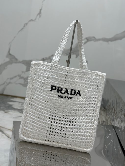 PRADA Crochet Tote Bag. Elevate your style with Prada's signature tote bag. This tote bag is the perfect addition to any summer wardrobe! Adorned with Prada's iconic triangle logo and embroidered lettering, its soft, deconstructed design is made with a light and natural raffia-effect yarn. It's sure to add an elevated touch to your ensemble.