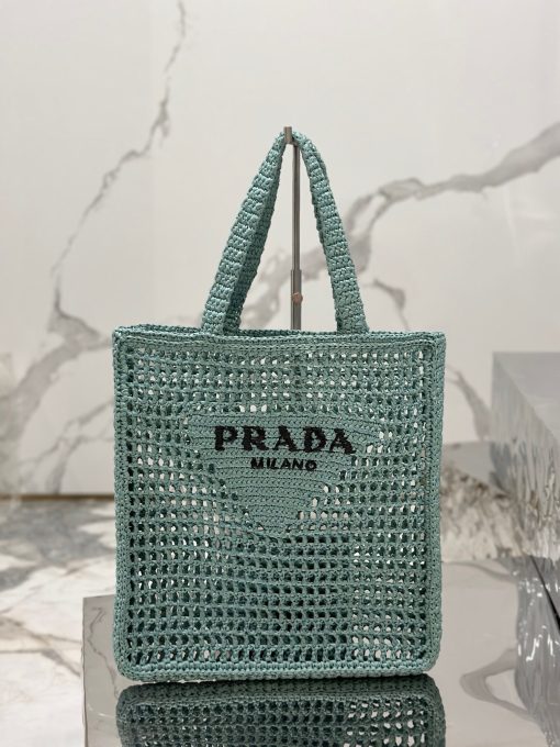 PRADA Crochet Tote Bag. Elevate your style with Prada's signature tote bag. This tote bag is the perfect addition to any summer wardrobe! Adorned with Prada's iconic triangle logo and embroidered lettering, its soft, deconstructed design is made with a light and natural raffia-effect yarn. It's sure to add an elevated touch to your ensemble.