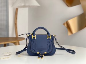 CHLOÉ Marcie Mini Double Carry Bag: Elegance in Miniature. Introducing a charming, petite rendition of the iconic Marcie handbag, this mini double carry bag exudes elegance with its meticulous craftsmanship in grained calfskin. Its clean, sleek lines and gracefully contoured design elevate the relaxed, slouchy silhouette, while the hand-wrapped leather handles impart an artisanal touch. The addition of metallic buckles bestows a polished and refined finish to this exquisite creation. Equipped with both double handles and a long, detachable shoulder strap, this mini bag epitomizes versatility, making it a must-have accessory for any occasion.