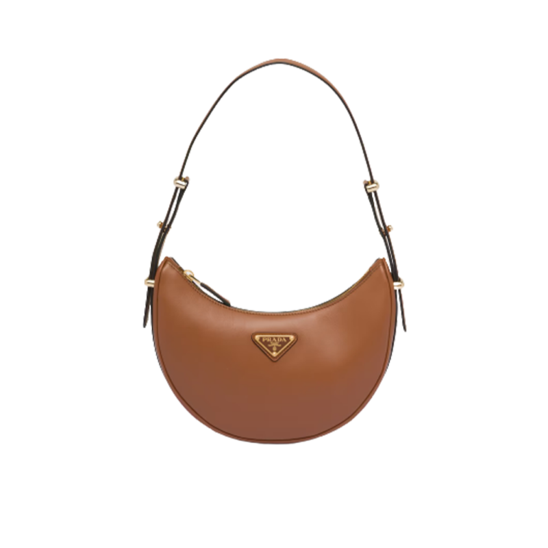 PRADA Leather Shoulder Bag. High-End Quality Bag including gift box, care book, dust bag, authenticity card. This sleek leather bag expresses versatile, modernist allure. The accessory with a curvy silhouette is completed by the leather extension for versatile wear. With a nappa leather lining and metal hardware, the bag is accented with the iconic enameled metal triangle logo on the front.