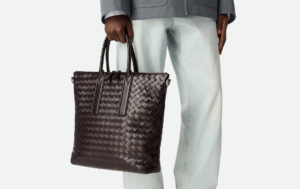 Luxury men’s bags – PRADA Brique Leather Bag and GUCCI GG Supreme Messenger displayed on a sleek marble table.