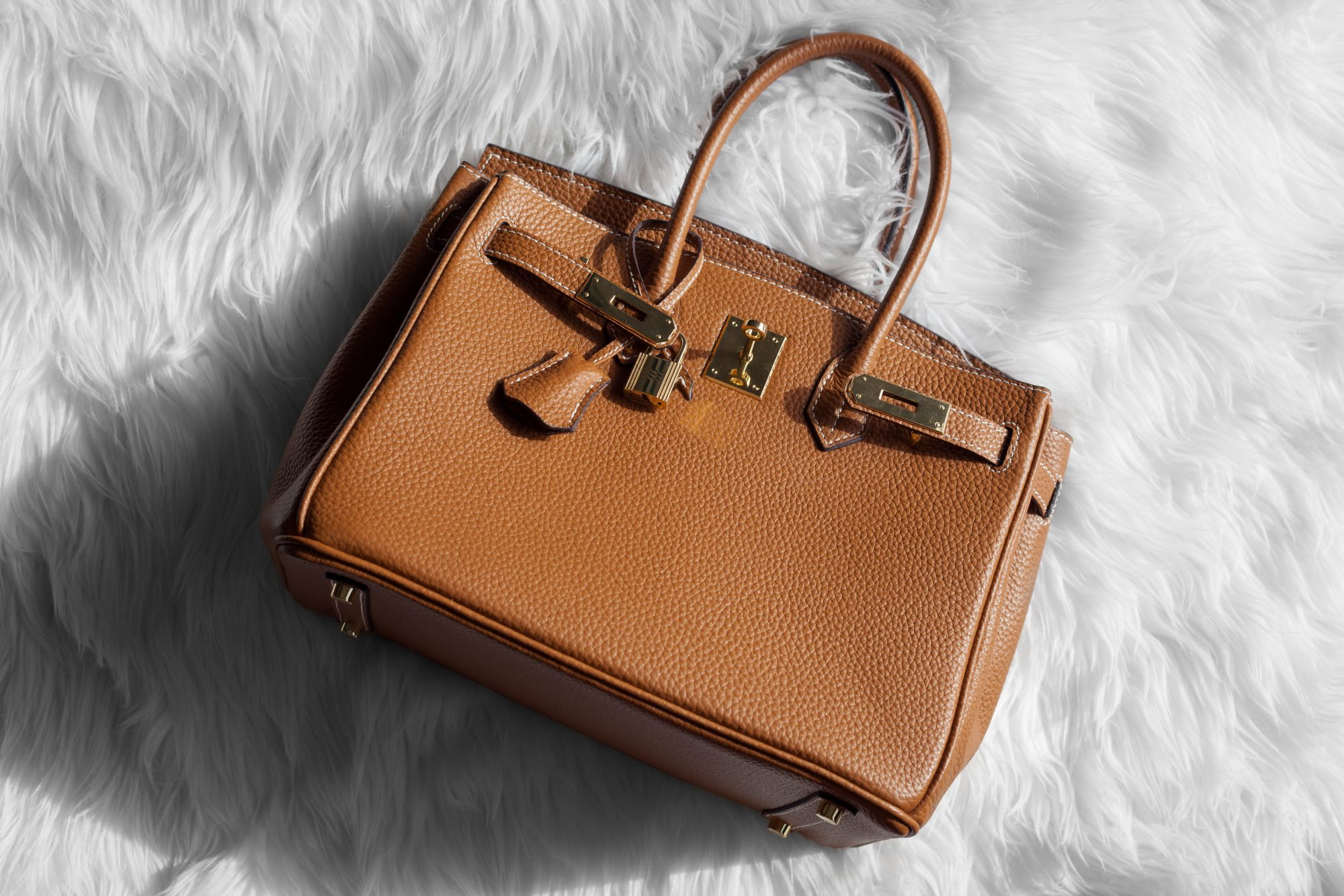 A tan HERMÈS Birkin bag displayed under soft boutique lighting, whispering promises of exclusivity to its future owner.