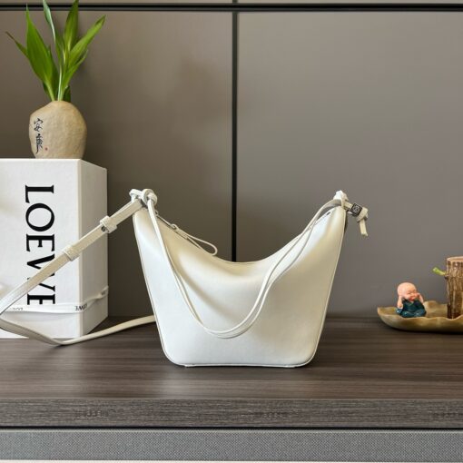 Mini Hammock Hobo. Authentic quality luxury bag crafted in genuine leather comes with authenticity card, dust bag and gift bag. Effortless Form, Everyday Function. The Mini Hammock Hobo is a contemporary reimagining of *oewe’s iconic Hammock bag. This streamlined variation offers a sleek, sculptural silhouette designed as a versatile sling bag for modern living. Expertly crafted in classic calfskin, it features soft, supple leather and a compact form that adapts effortlessly to your day. The unique design allows for multiple carry options—wear it crossbody, over the shoulder, or by hand. Elegant yet functional, this mini hobo is perfect for essentials, making it an ideal choice for both daily wear and minimalist style statements.