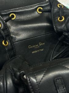 Small Caro Backpack. Authentic quality luxury bag crafted in genuine leather comes with authenticity card, dust bag and gift bag. Elegance Meets Effortless Edge. Elevate your everyday with the Small Caro Backpack — a flawless blend of modern femininity and iconic House craftsmanship. Luxuriously crafted in lambskin, its supple silhouette is enhanced by bold Macrocannage topstitching that whispers timeless *ior style. The antique gold-finish ‘CD’ clasp opens to a drawstring main compartment, perfectly balancing beauty and practicality. A discreet flap pocket keeps your daily essentials close at hand, while the top handle and adjustable leather straps offer versatile, all-day comfort. Whether slung over your shoulder or carried by hand, this petite powerhouse delivers Parisian polish in every step.