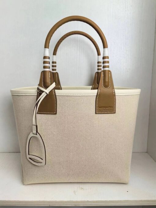 Steeple 25 Bag. Authentic quality luxury bag crafted in genuine leather comes with authenticity card, dust bag and gift bag. Where art meets heritage. The *rmès Steeple Bag is a charming fusion of heritage and artistry, crafted from a blend of canvas and Swift leather. Its design pays tribute to *rmès’ equestrian roots with whip-shaped handles and a stirrup-inspired charm, adding a playful yet sophisticated touch. Lightweight yet spacious, the Steeple is ideal for daily use. Whether you opt for a vibrant motif or a sleek, single-color design, this bag stands out as an artistic expression of luxury that seamlessly integrates into a modern lifestyle. Praised for its unique aesthetic and accessibility within the *rmès lineup, the Steeple Bag is adored by fashion enthusiasts who appreciate its colorful palette and bold personality. While it’s best suited for those who enjoy the texture and look of canvas, it remains a versatile statement piece that captures the spirit of everyday elegance.