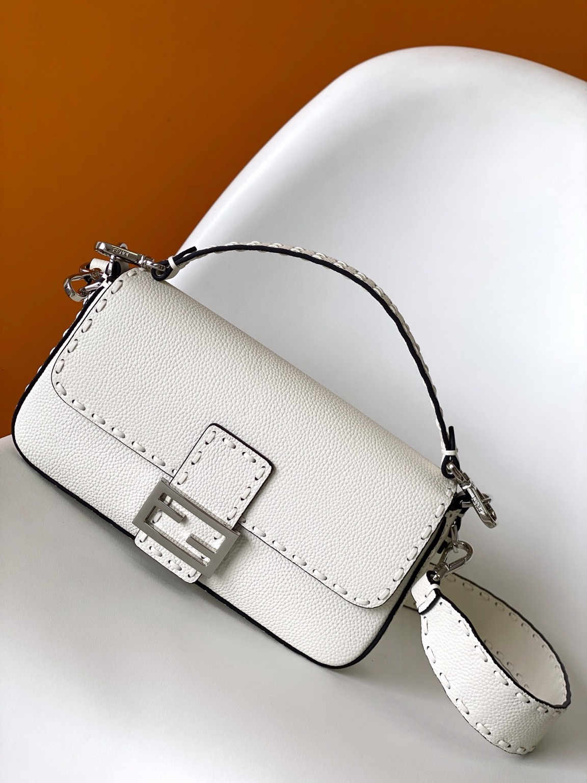 Baguette Medium 13 Baguette Medium. Authentic quality luxury bag crafted in genuine leather comes with authenticity card, dust bag and gift bag. A Legacy in Every Stitch. An icon, reimagined with artisanal mastery—the *ENDI Medium Baguette is a tribute to heritage and timeless design. Crafted in rich cappuccino Cuoio Romano leather, this piece features 612 hand-sewn tone-on-tone macro topstitches, showcasing the legendary Selleria craftsmanship passed down since 1925. Its structured silhouette is elevated by the signature FF clasp, while the soft calfskin interior, complete with a zip pocket, keeps essentials elegantly organized. Finished with a silver Selleria plaque and palladium-finish hardware, every detail speaks of quiet luxury. Versatility meets sophistication with a detachable handle and shoulder strap, allowing it to be carried by hand, worn on the shoulder, or styled cross-body. A true icon—crafted by hand, designed to last a lifetime.