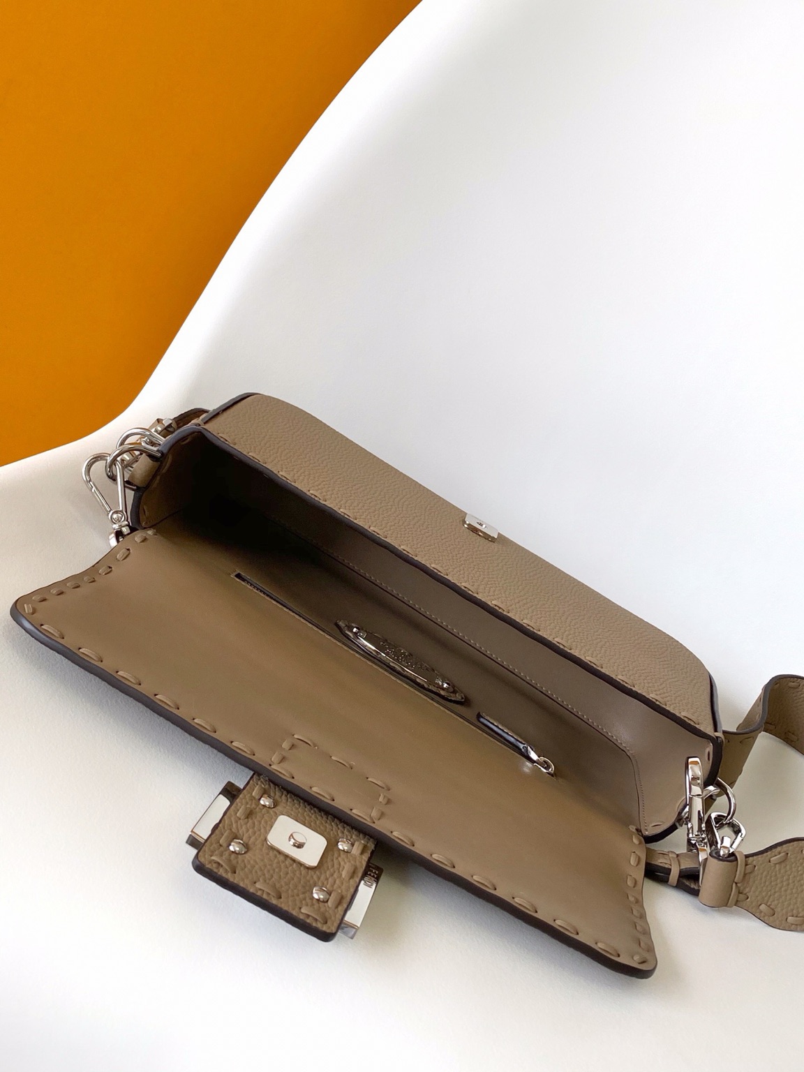 Baguette Medium 9 Baguette Medium. Authentic quality luxury bag crafted in genuine leather comes with authenticity card, dust bag and gift bag. A Legacy in Every Stitch. An icon, reimagined with artisanal mastery—the *ENDI Medium Baguette is a tribute to heritage and timeless design. Crafted in rich cappuccino Cuoio Romano leather, this piece features 612 hand-sewn tone-on-tone macro topstitches, showcasing the legendary Selleria craftsmanship passed down since 1925. Its structured silhouette is elevated by the signature FF clasp, while the soft calfskin interior, complete with a zip pocket, keeps essentials elegantly organized. Finished with a silver Selleria plaque and palladium-finish hardware, every detail speaks of quiet luxury. Versatility meets sophistication with a detachable handle and shoulder strap, allowing it to be carried by hand, worn on the shoulder, or styled cross-body. A true icon—crafted by hand, designed to last a lifetime.