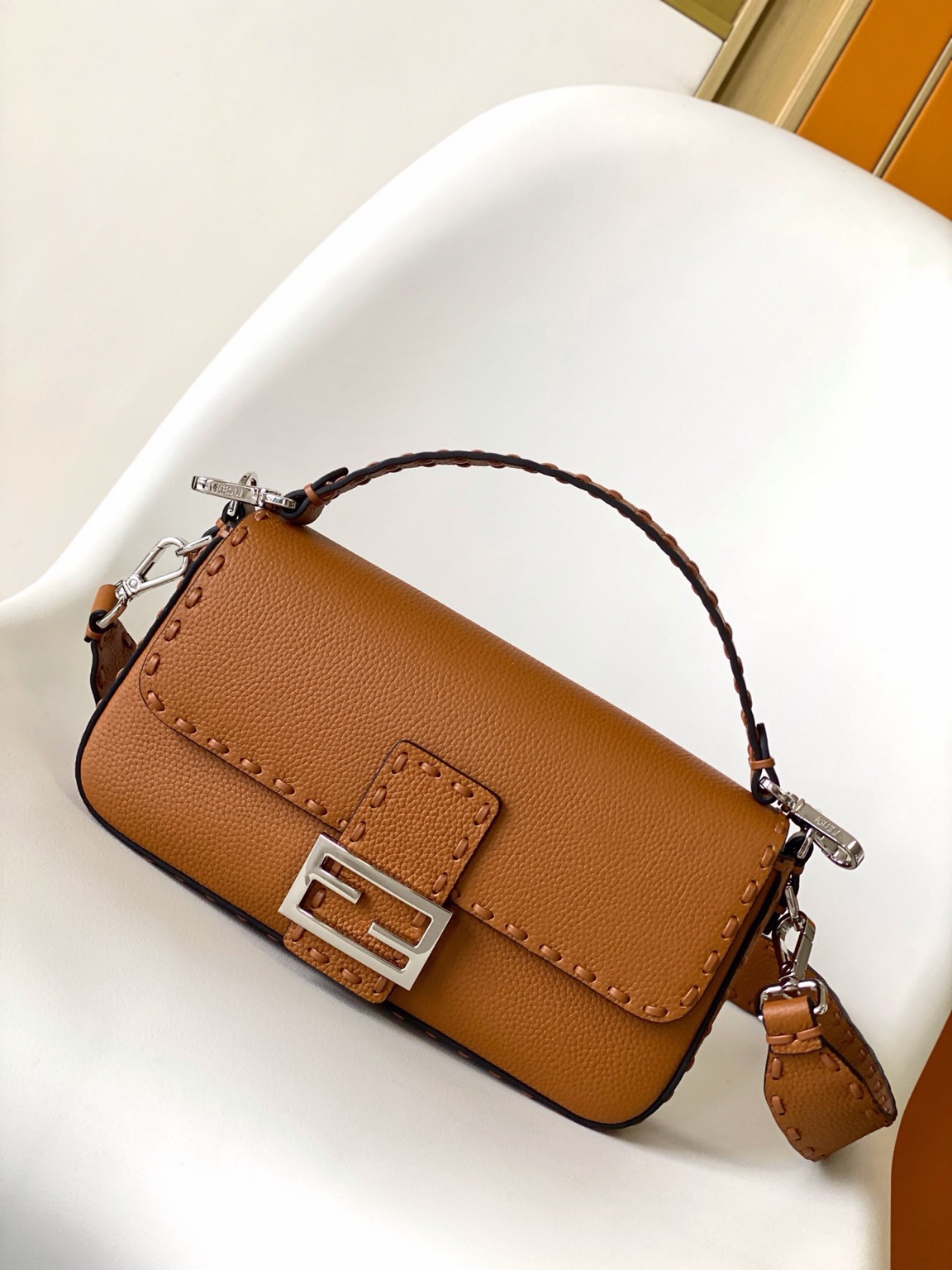Baguette Medium 11 Baguette Medium. Authentic quality luxury bag crafted in genuine leather comes with authenticity card, dust bag and gift bag. A Legacy in Every Stitch. An icon, reimagined with artisanal mastery—the *ENDI Medium Baguette is a tribute to heritage and timeless design. Crafted in rich cappuccino Cuoio Romano leather, this piece features 612 hand-sewn tone-on-tone macro topstitches, showcasing the legendary Selleria craftsmanship passed down since 1925. Its structured silhouette is elevated by the signature FF clasp, while the soft calfskin interior, complete with a zip pocket, keeps essentials elegantly organized. Finished with a silver Selleria plaque and palladium-finish hardware, every detail speaks of quiet luxury. Versatility meets sophistication with a detachable handle and shoulder strap, allowing it to be carried by hand, worn on the shoulder, or styled cross-body. A true icon—crafted by hand, designed to last a lifetime.